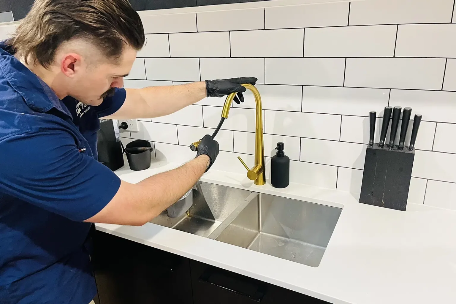 A professional Plumber repairs a golden Kitchen Tap with a hose. Kitchen Tap Repairs on the Gold Coast - High Tide Plumbing & Gas