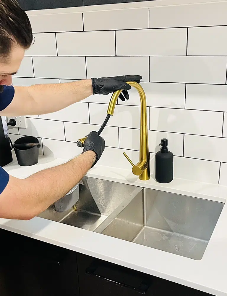 A professional Plumber repairs a golden Kitchen Tap with a hose. Kitchen Tap Repairs on the Gold Coast - High Tide Plumbing & Gas