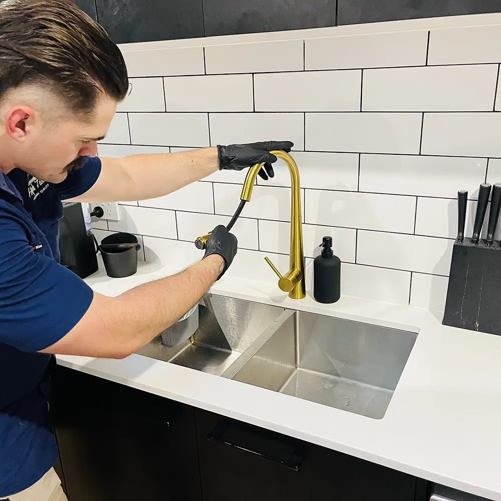 A professional Plumber repairs a golden Kitchen Tap with a hose. Kitchen Tap Repairs on the Gold Coast - High Tide Plumbing & Gas