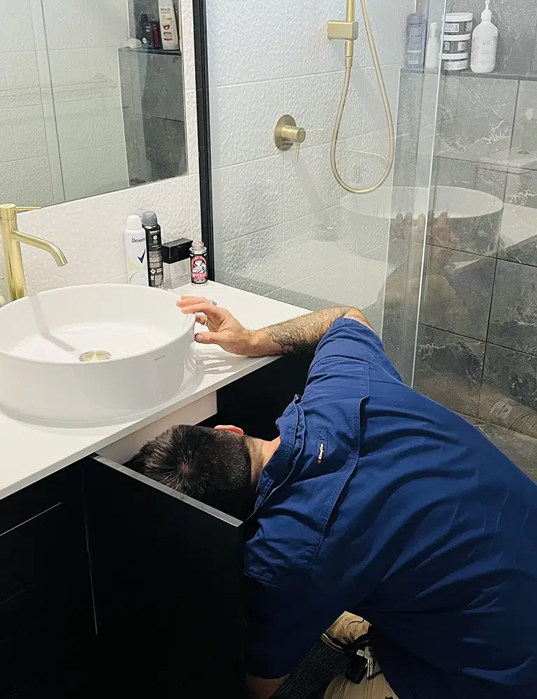 A Professional Plumber with his head under a sink for moisture. Leak Detection on The Gold Coast - High Tide Plumbing & Gas Gold Coast
