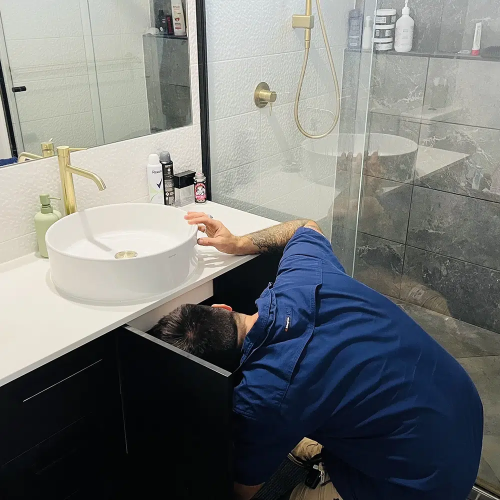 A Professional Plumber with his head under a sink for moisture. Leak Detection on The Gold Coast - High Tide Plumbing & Gas Gold Coast