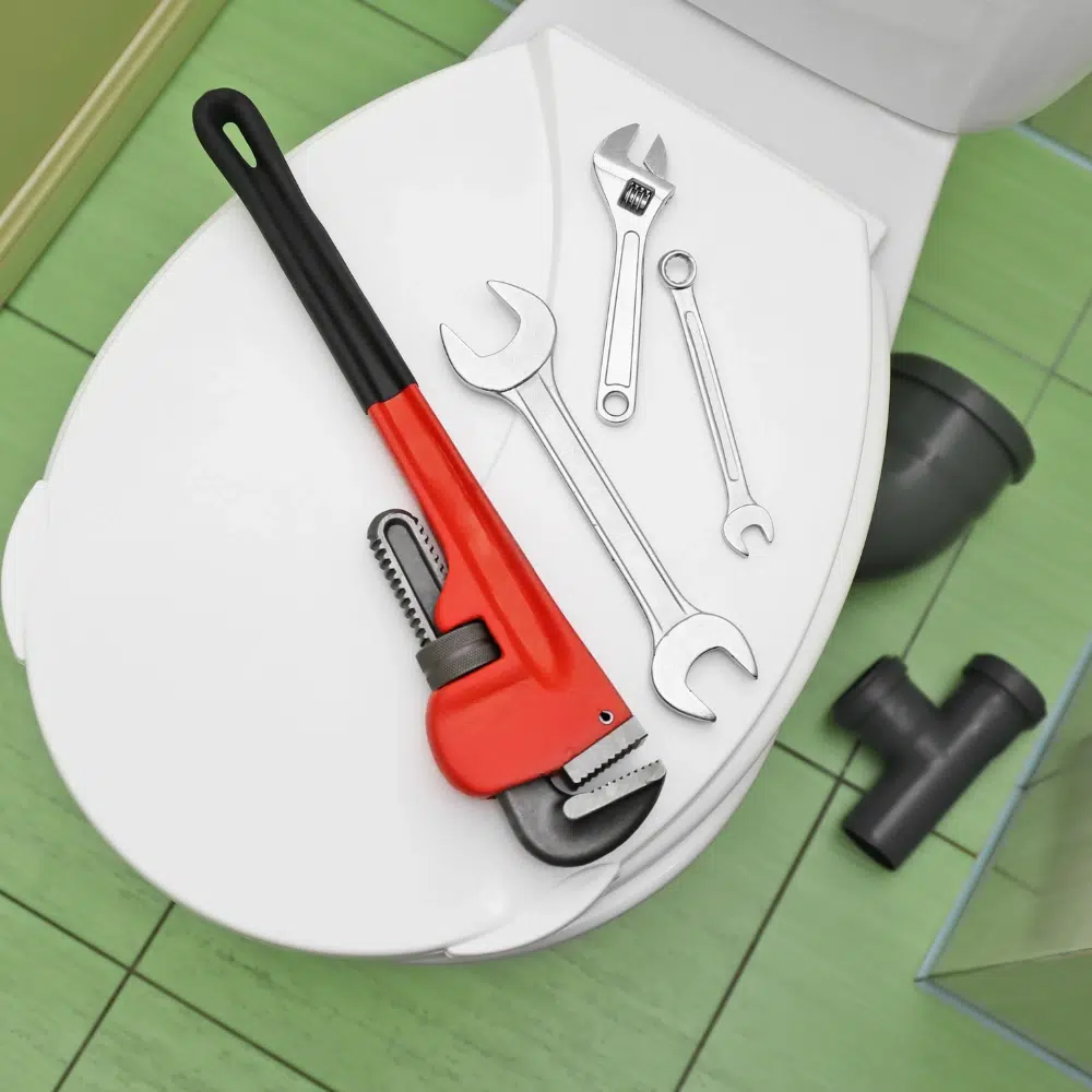 A selection of plumbing tools on the toilet lid with a green tiled floor as a licenced plumber prepares for Toilet Repairs on the Gold Coast