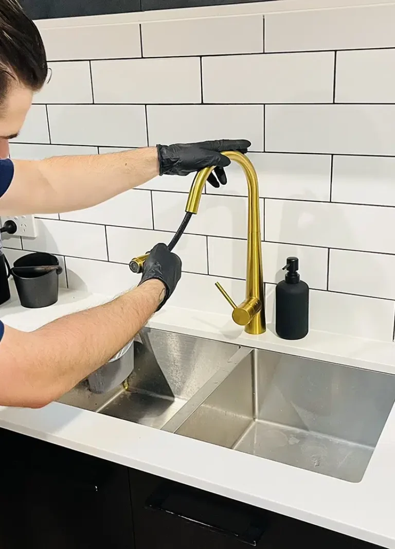 A professional Plumber repairs a golden Kitchen Tap with a hose. Kitchen Tap Repairs on the Gold Coast - High Tide Plumbing & Gas