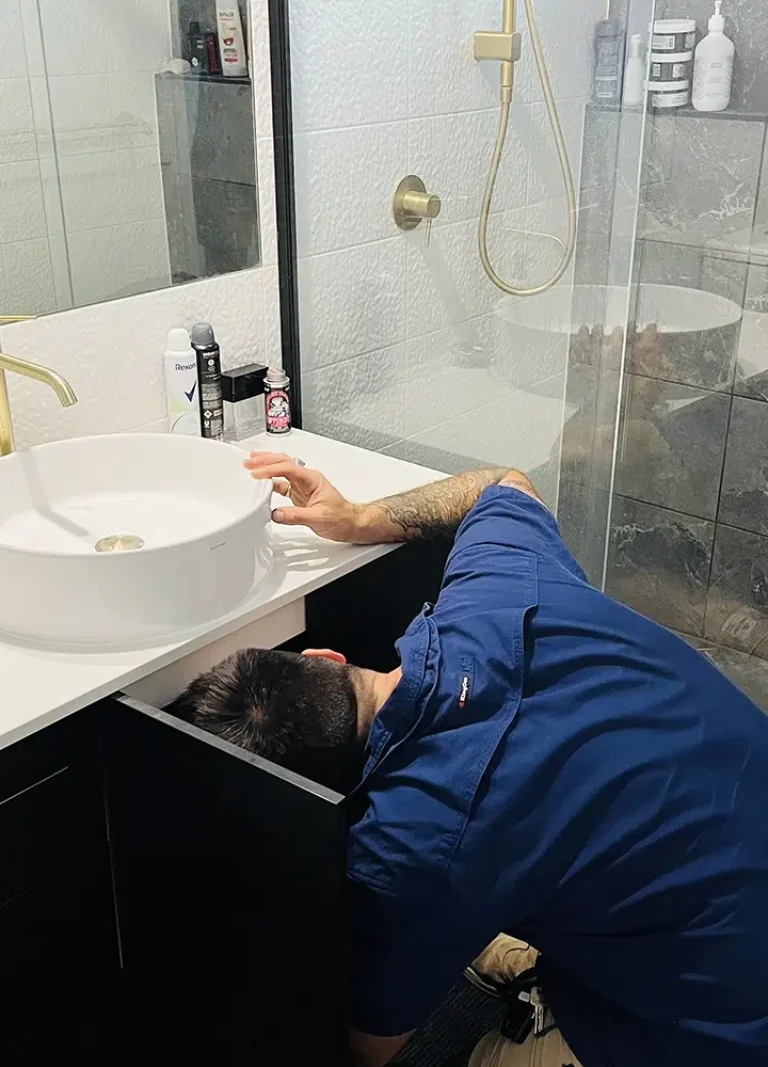 A Professional Plumber with his head under a sink for moisture. Leak Detection on The Gold Coast - High Tide Plumbing & Gas Gold Coast